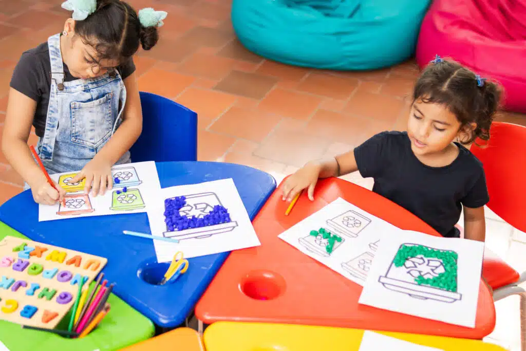 Two young children colouring in EFL worksheets at colourful kindergarten tables