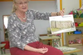 Older teacher Sandra seated, showing a flashcard to her students
