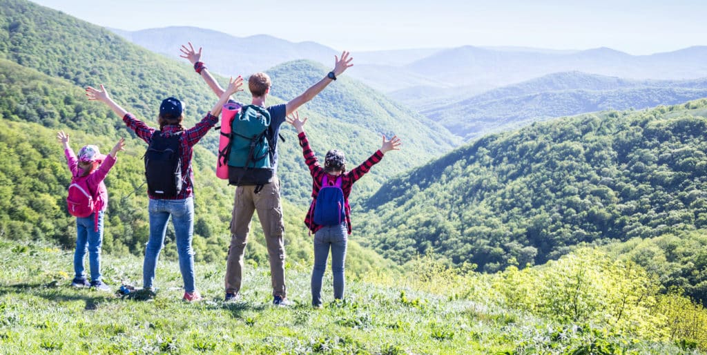 Family of four holds hands high at the end of a hike at the top of a mountain