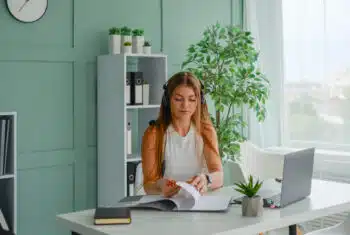 Teacher at a desk teaching online, with plants behind her
