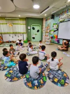 Chinese Young Learners sitting on the floor listening to their teacher