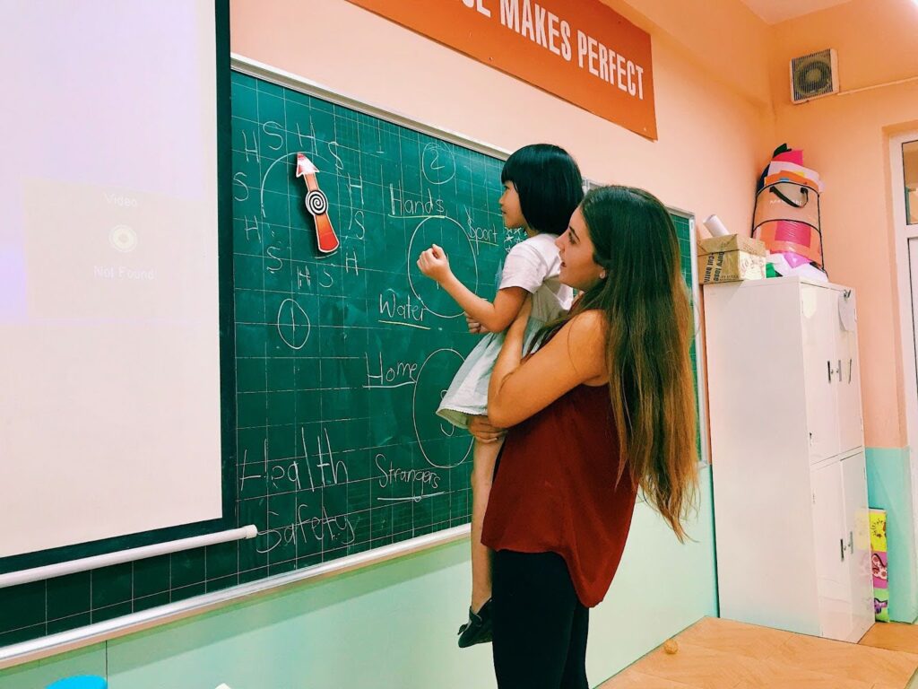 Teacher Taylor holding a young student up to write on a blackboard in Vietnam