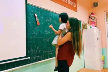 Teacher Taylor holding a young student up to write on a blackboard in Vietnam
